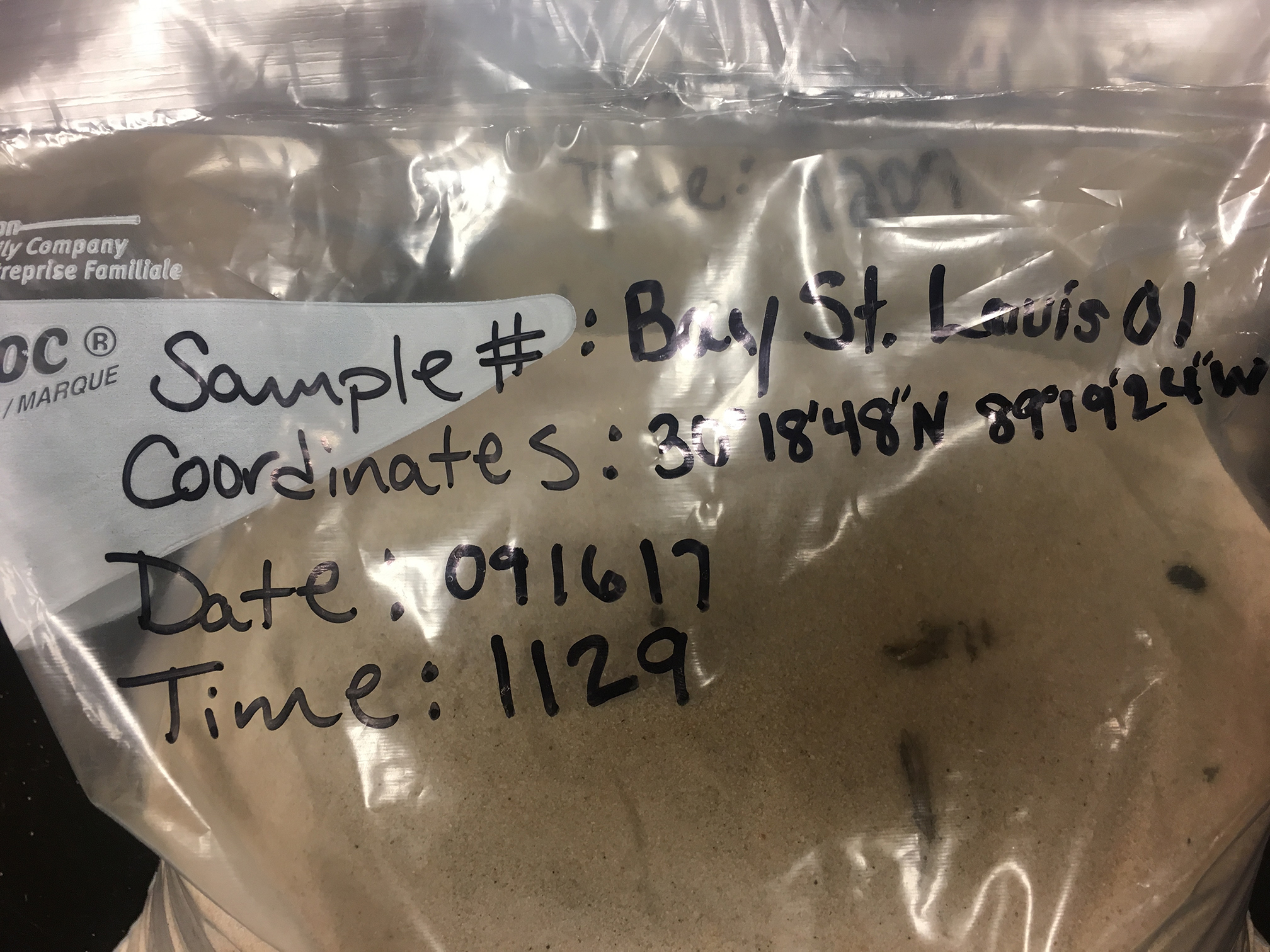 The labeled bag of sand includes the sample number, coordinates, and the date and time.